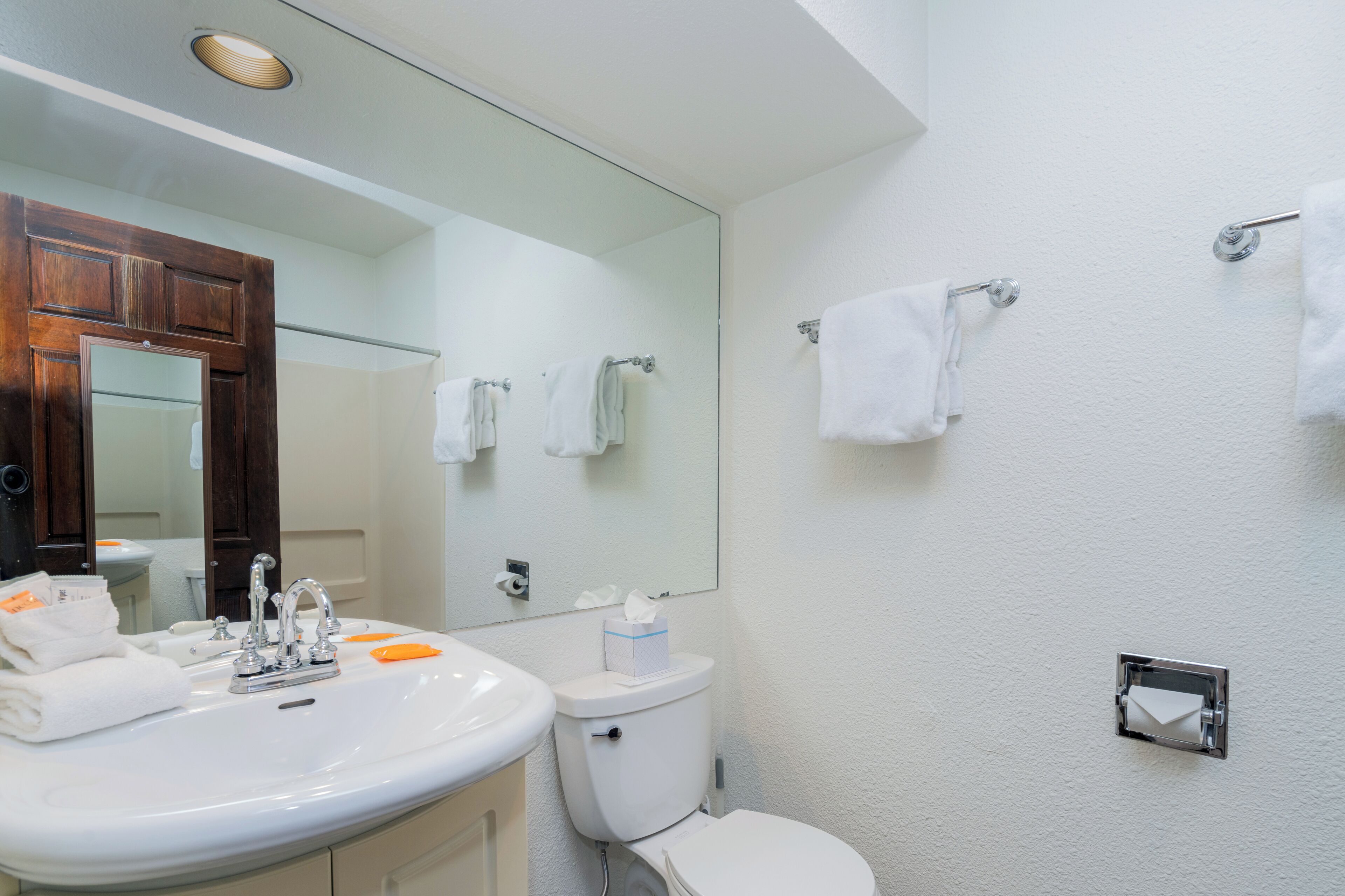 A bathroom with a sink, mirror, toilet, and towel racks.