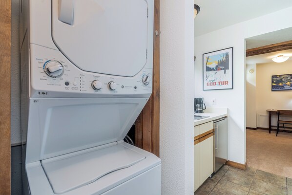 A laundry area with a washing machine, a coffee maker, and a dining area with a table and chairs. - Clean, Spacious Suite in Prime Riverside Location (Telluride)