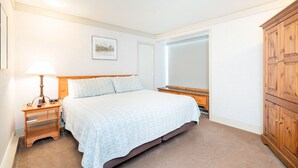 Quarto com cama, mesa de cabeceira, abajur e guarda-roupa de madeira.