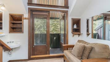 A room with a wooden bench, a sofa, a sink, and a door leading to a balcony.
