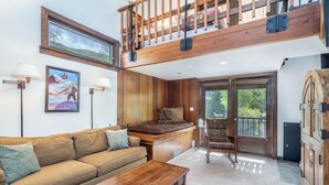 A loft-style room with a wooden ceiling, a sofa, a wooden table, a bar area, and a large window.