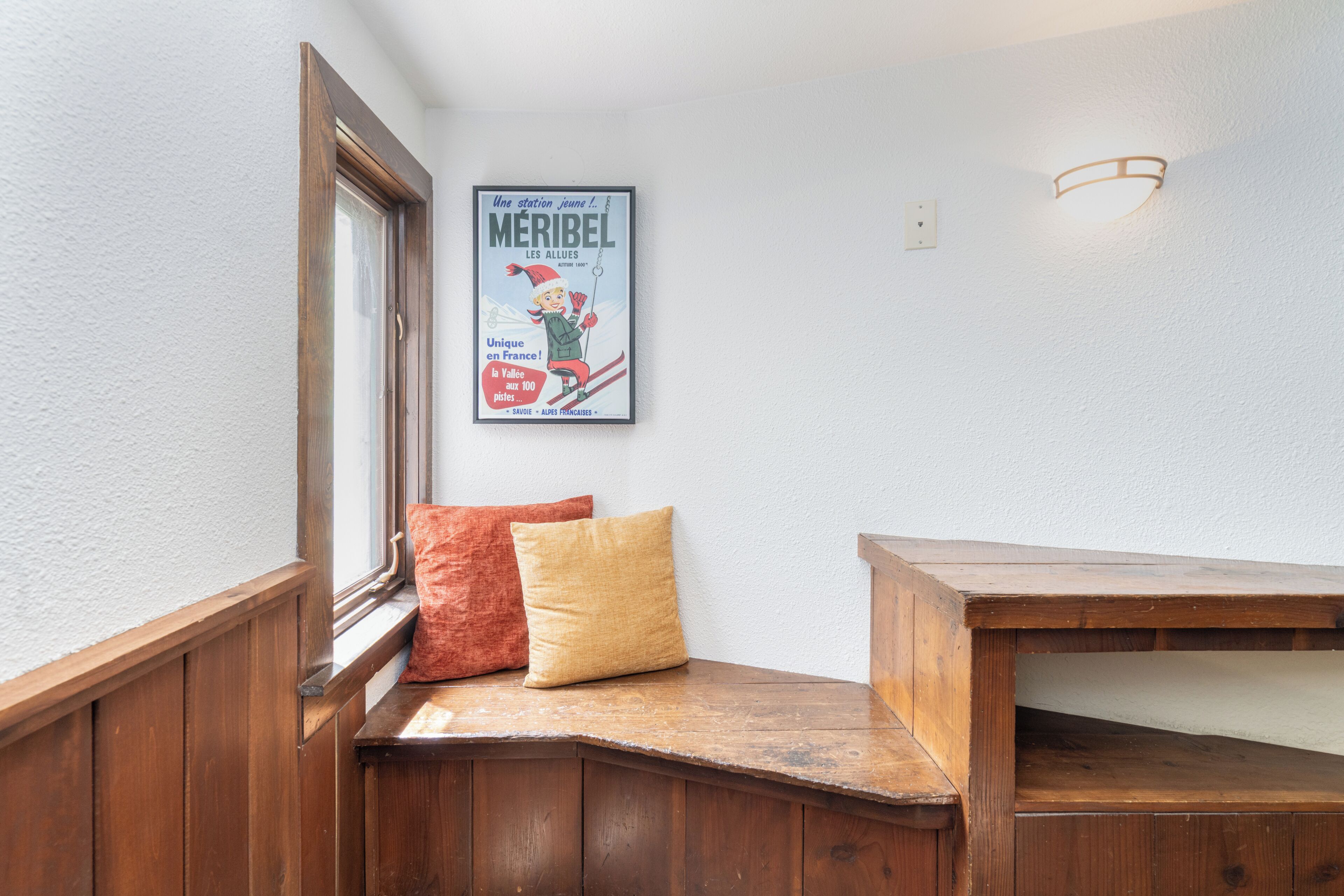 A corner with a wooden bench, a poster on the wall, and a window with a view.