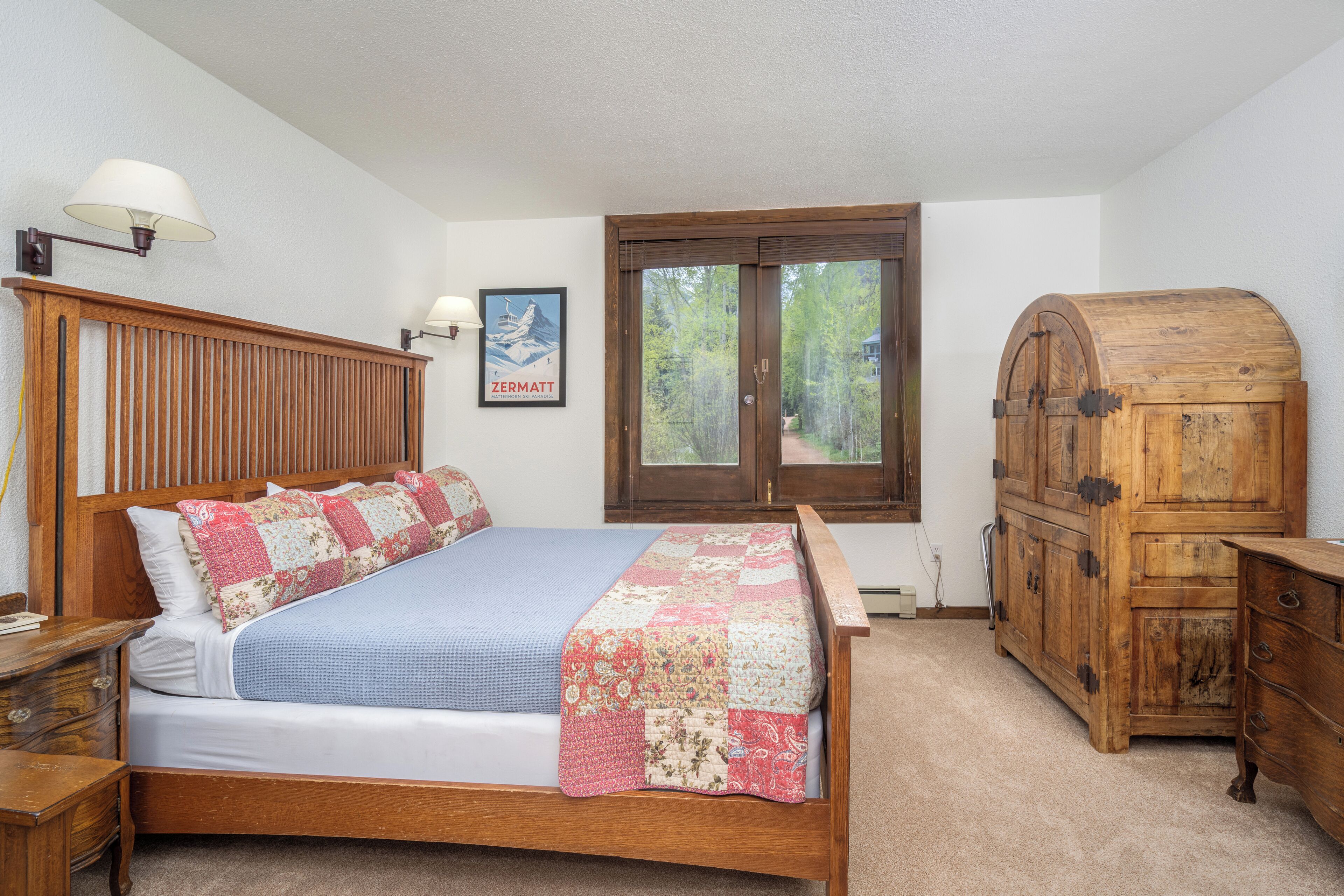 A bedroom with a wooden bed, a nightstand, a dresser, and a window with a view of trees.
