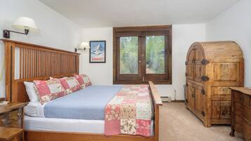 A bedroom with a wooden bed, a nightstand, a dresser, and a window with a view of trees.