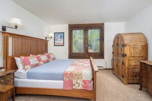 A bedroom with a wooden bed, a nightstand, a dresser, a window with a view, and a wall-mounted lamp. - Hotel Room on the San Miguel River in Quintessential Lodge (Telluride)