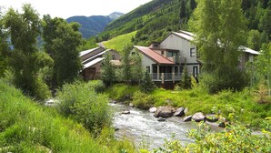 Ein Haus mit Veranda, das auf einen Fluss mit Blick auf üppiges Grün und Berge blickt.