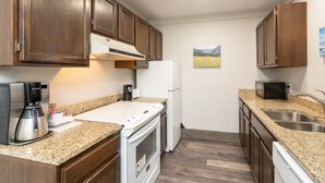 A kitchen with wooden cabinets, a white refrigerator, a microwave, a toaster, and a granite countertop.
