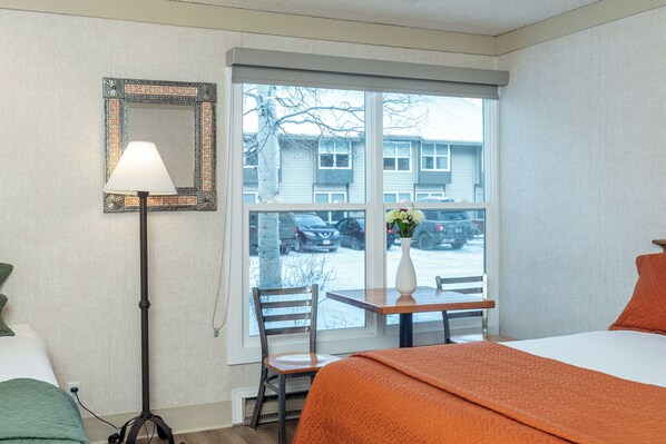 Een hotelkamer met een bed, een bureau met stoel, een lamp en een raam met uitzicht.
