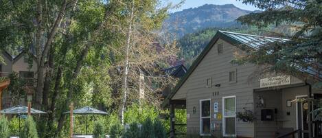 A mountain lodge with a welcoming sign, surrounded by lush greenery and a view of mountains.