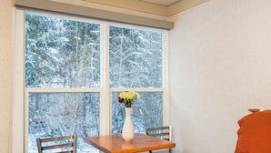 A room with a wooden table and chairs, a white vase with flowers, and a large window with a snowy view. - Mountainside Inn Room With Kitchenette (Telluride)