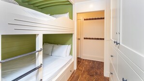 Un lit superposé avec une tête de lit verte, une porte blanche avec un porte-manteau et un plancher en bois.
