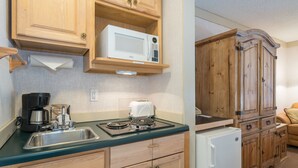 A kitchen with wooden cabinets, a microwave, a toaster, a coffee maker, and a refrigerator. - Mountainside Inn Hotel Room With Kitchenette and Sitting Area (Telluride)
