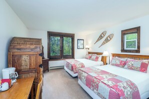 A bedroom with two beds, a wooden cabinet, a coffee maker, and a window with a view of trees.