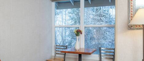 A corner room with a window, a table with chairs, and a vase with flowers.