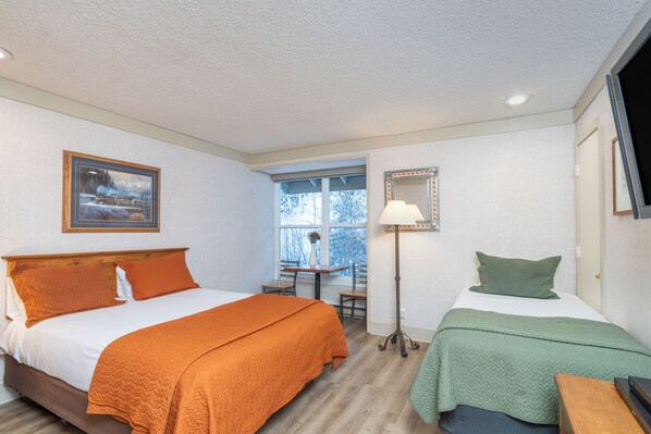 A hotel room with two beds, a window, a desk, and a lamp.
