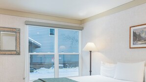 A hotel room with a bed, a window with a view of the outside, a lamp, and a framed picture on the wall. - Mountainside Inn Hotel Room With King Bed (Telluride)