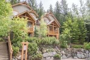 A lodge with a stone retaining wall, wooden balconies, and a staircase leading to the entrance. - Ski in & Out, Private Hot Tub, Free Shuttle (Whistler)