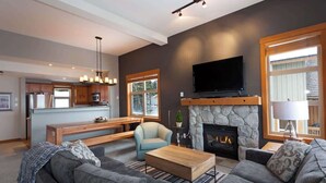 A modern living room with a fireplace, a television, and a kitchen in the background.