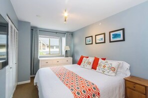 Um quarto com cama, janela, mesa de cabeceira e uma luminária fixada na parede.