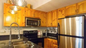A kitchen with wooden cabinets, stainless steel appliances, a granite countertop, and a hanging light fixture. - Gorgeous 2 Bed, Village location, Shared Hot Tub (Whistler)