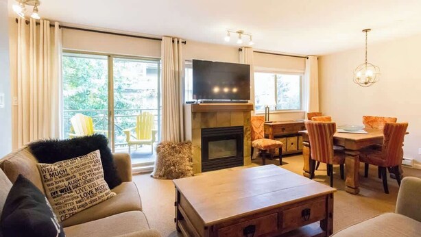 A living room with a fireplace, a television, and a dining area with chairs and a table. - Gorgeous 2 Bed, Village location, Shared Hot Tub (Whistler)