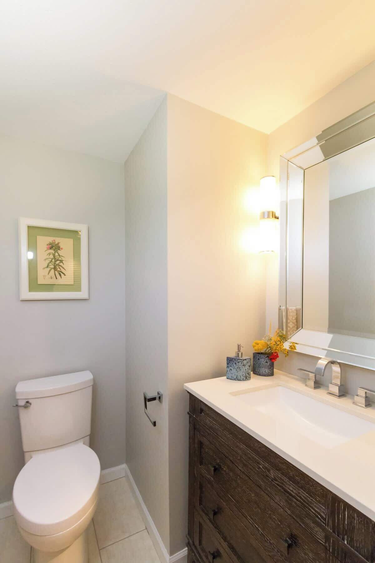 A bathroom with a toilet, a sink with a mirror, and a framed picture on the wall.