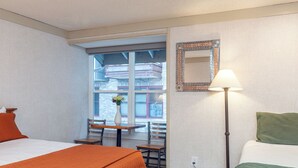 Une chambre d’hôtel avec un lit, un bureau et une chaise, une fenêtre donnant sur des immeubles et une lampe.