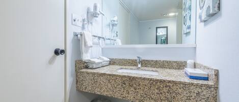 A bathroom with a granite countertop, a sink, a mirror, and a trash can.