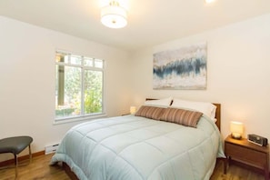 A bedroom with a bed, a window, a chair, and a nightstand with a lamp.