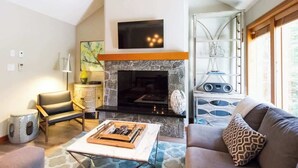 A living room with a fireplace, a sofa, a coffee table, and a television mounted above the fireplace. - Ski Home, Free Shuttle, Communal Hot Tub (Whistler)