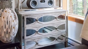 A room with a stone fireplace, a wooden shelf with a bicycle ornament, a book titled 'WHISTLER,' and a speaker unit labeled 'FLUANCE.' - Ski Home, Free Shuttle, Communal Hot Tub (Whistler)