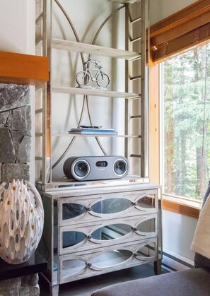 A room with a stone fireplace, a wooden shelf with a bicycle ornament, a book titled 'WHISTLER,' and a speaker unit labeled 'FLUANCE.'