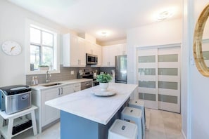 Une cuisine moderne avec des meubles blancs, un îlot central, un four à micro-ondes et un réfrigérateur.