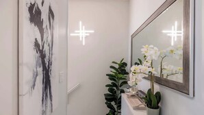 Un pasillo con una obra de arte moderna, un espejo grande y una planta en maceta.