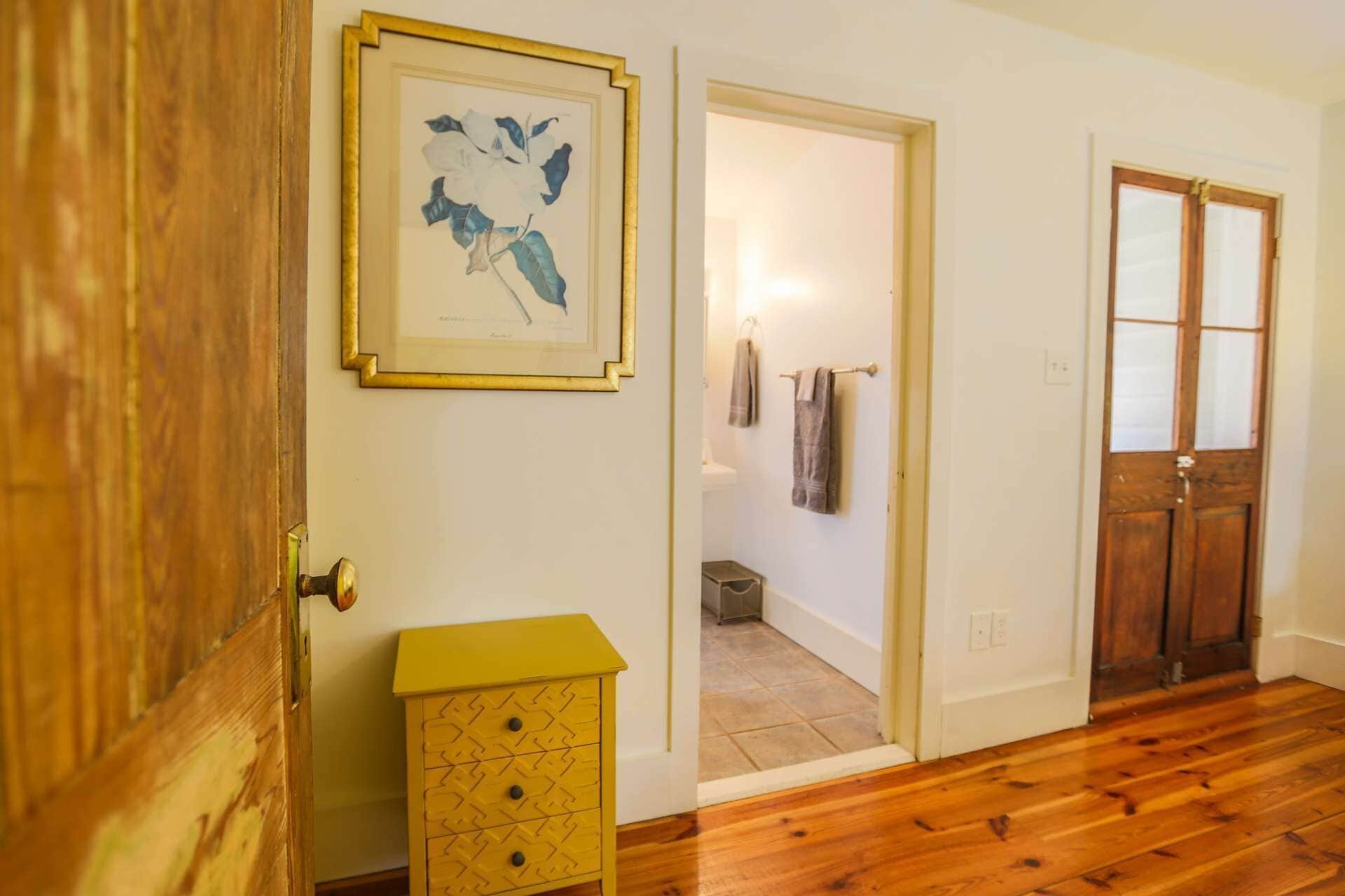 A hallway with wooden flooring, a yellow cabinet, and a framed botanical print on the wall.