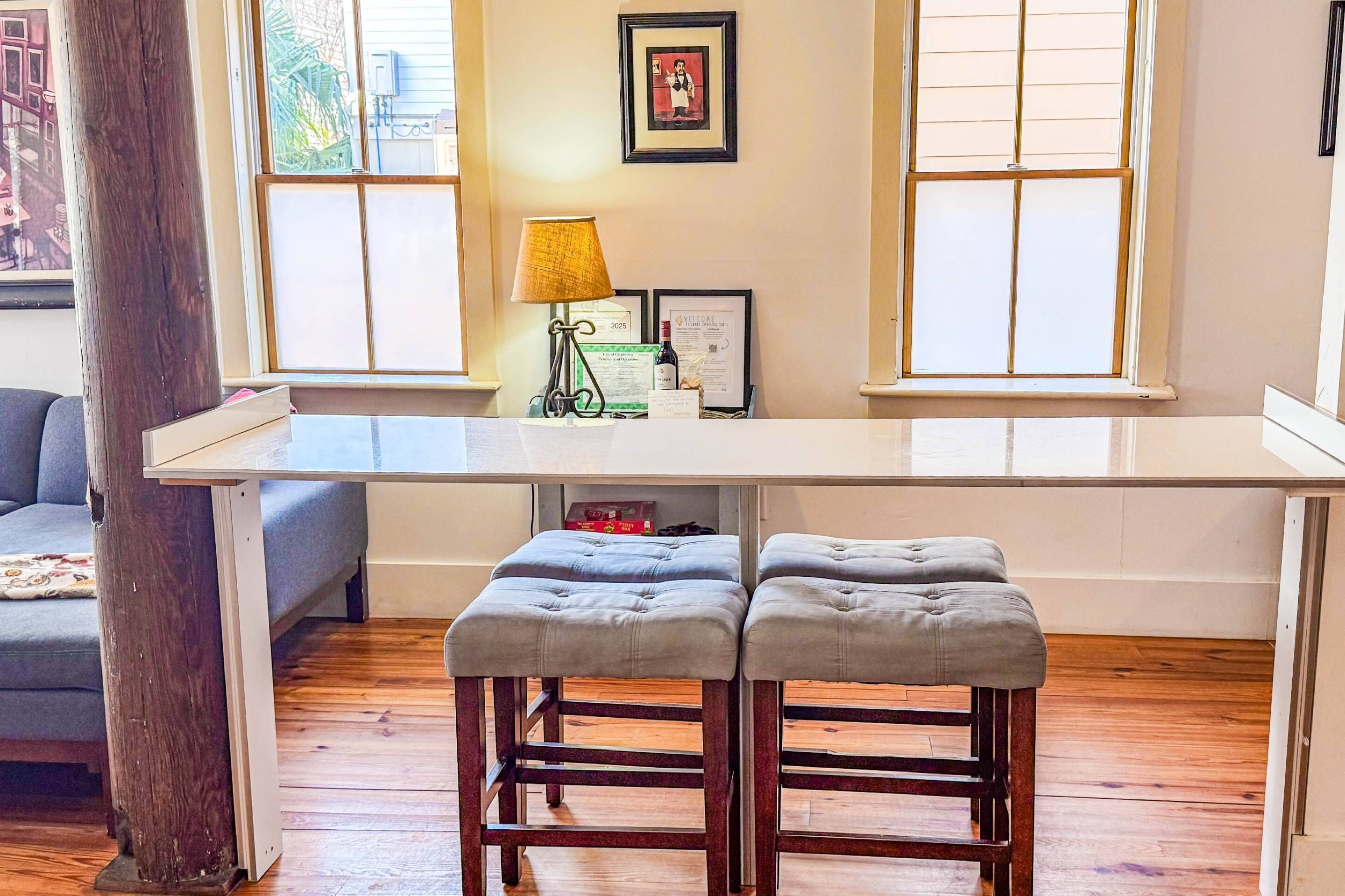 A modern kitchen with a white countertop, two barstools, a lamp, and framed certificates on the wall.
