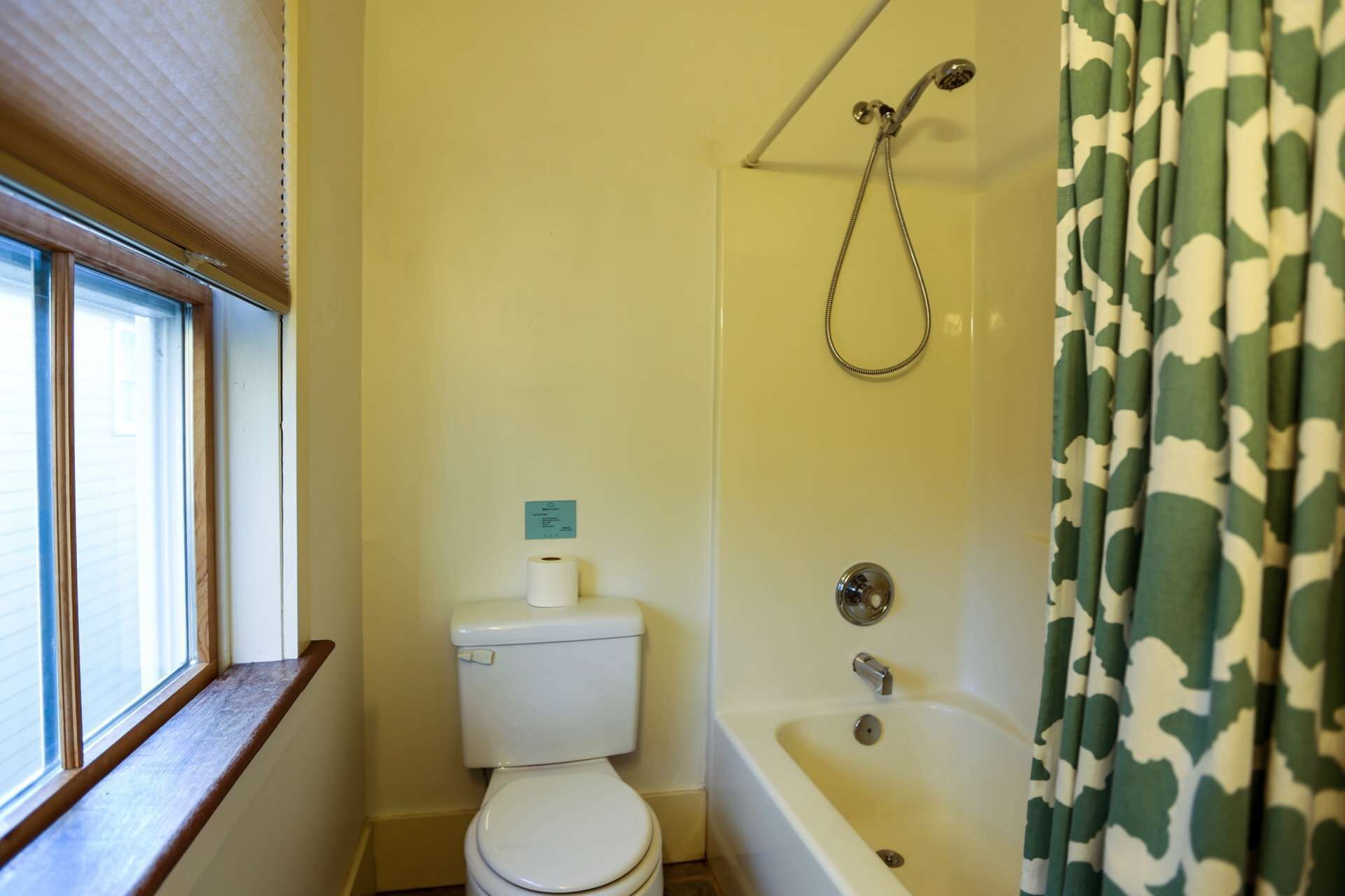 A bathroom with a toilet, a shower with a curtain, and a window with blinds.