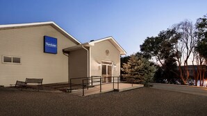 Un hotel Travelodge con fachada color beige, una banca afuera y un camino de entrada de grava.