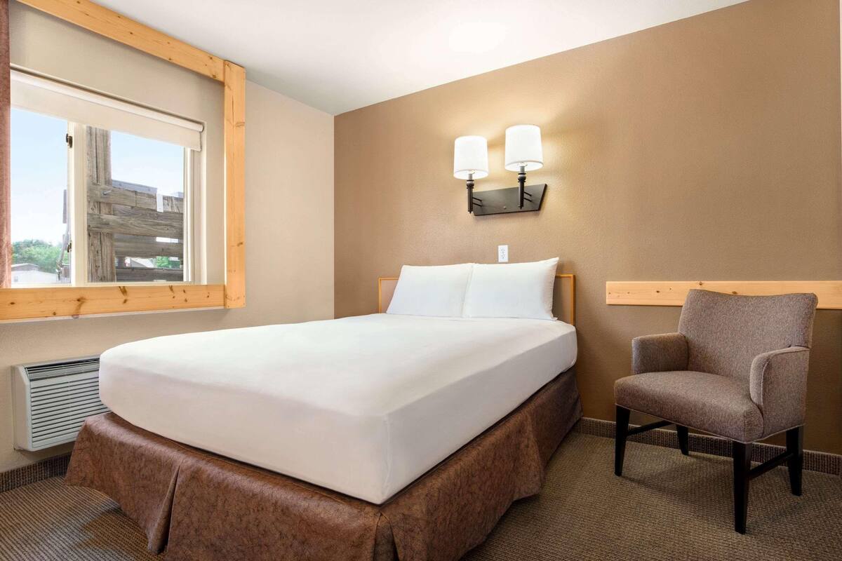 Una habitación de hotel con una cama grande, una silla, un ventanal y lámparas fijadas a la pared.