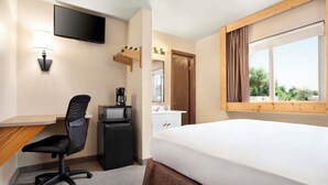 Habitación de hotel con cama, escritorio, silla, televisor, cafetera y ventana con vistas.