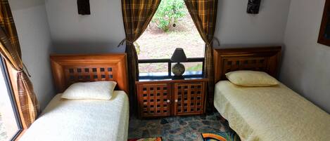 Una habitación con dos camas de madera, una mesita con una lámpara y una ventana con cortinas.