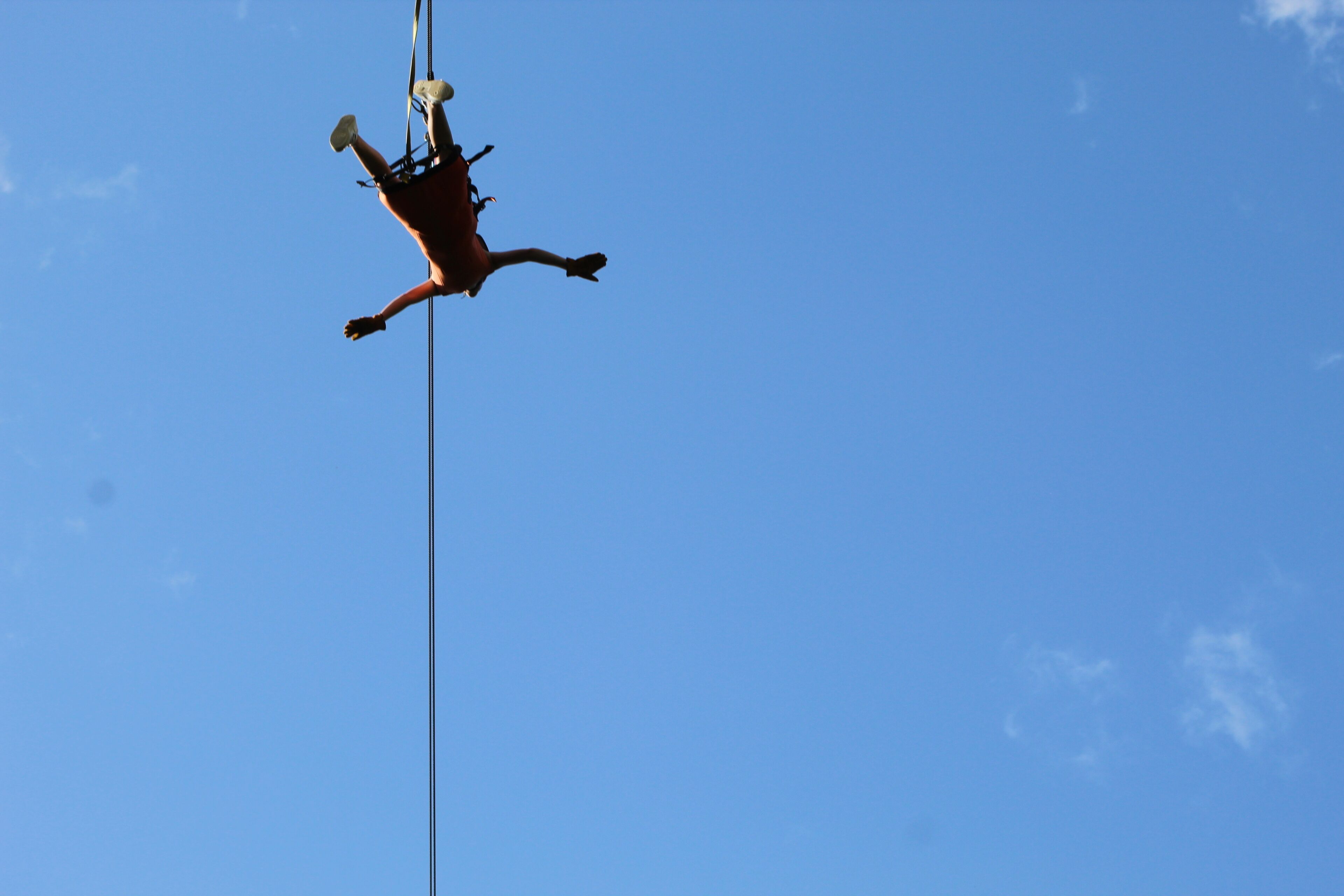 A person suspended in mid-air, attached to a rope against a clear blue sky.