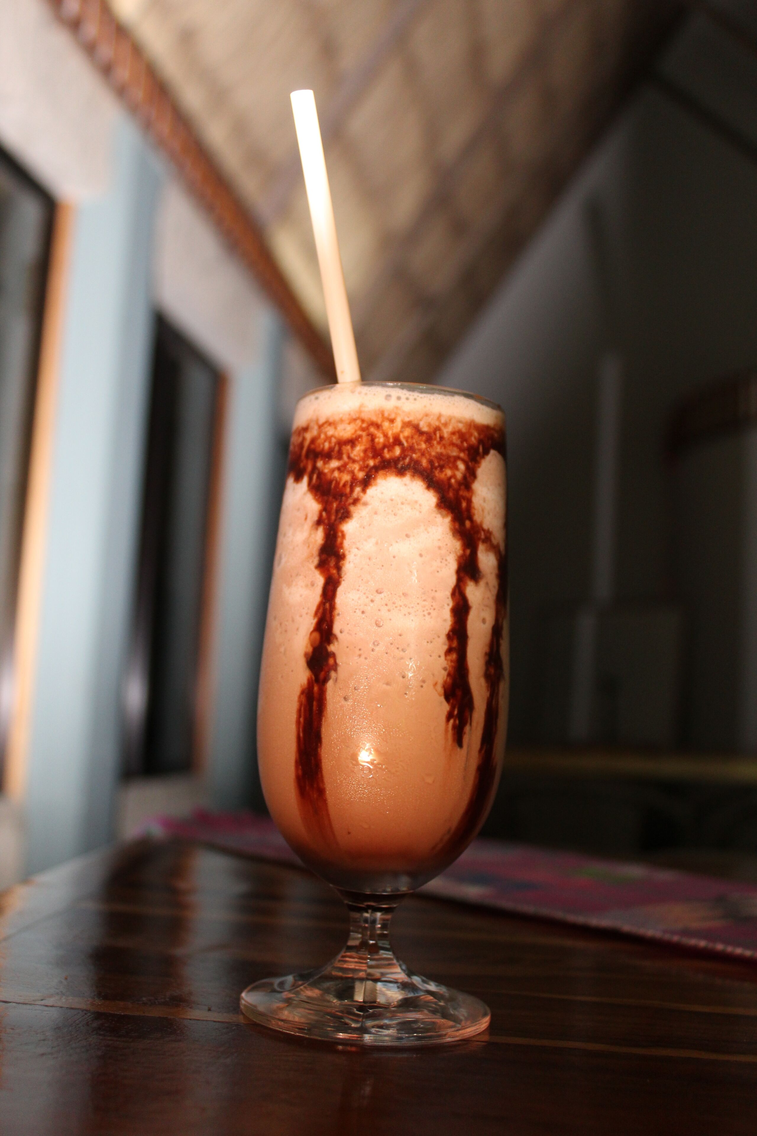 A glass of chocolate milkshake with a straw, placed on a wooden table.
