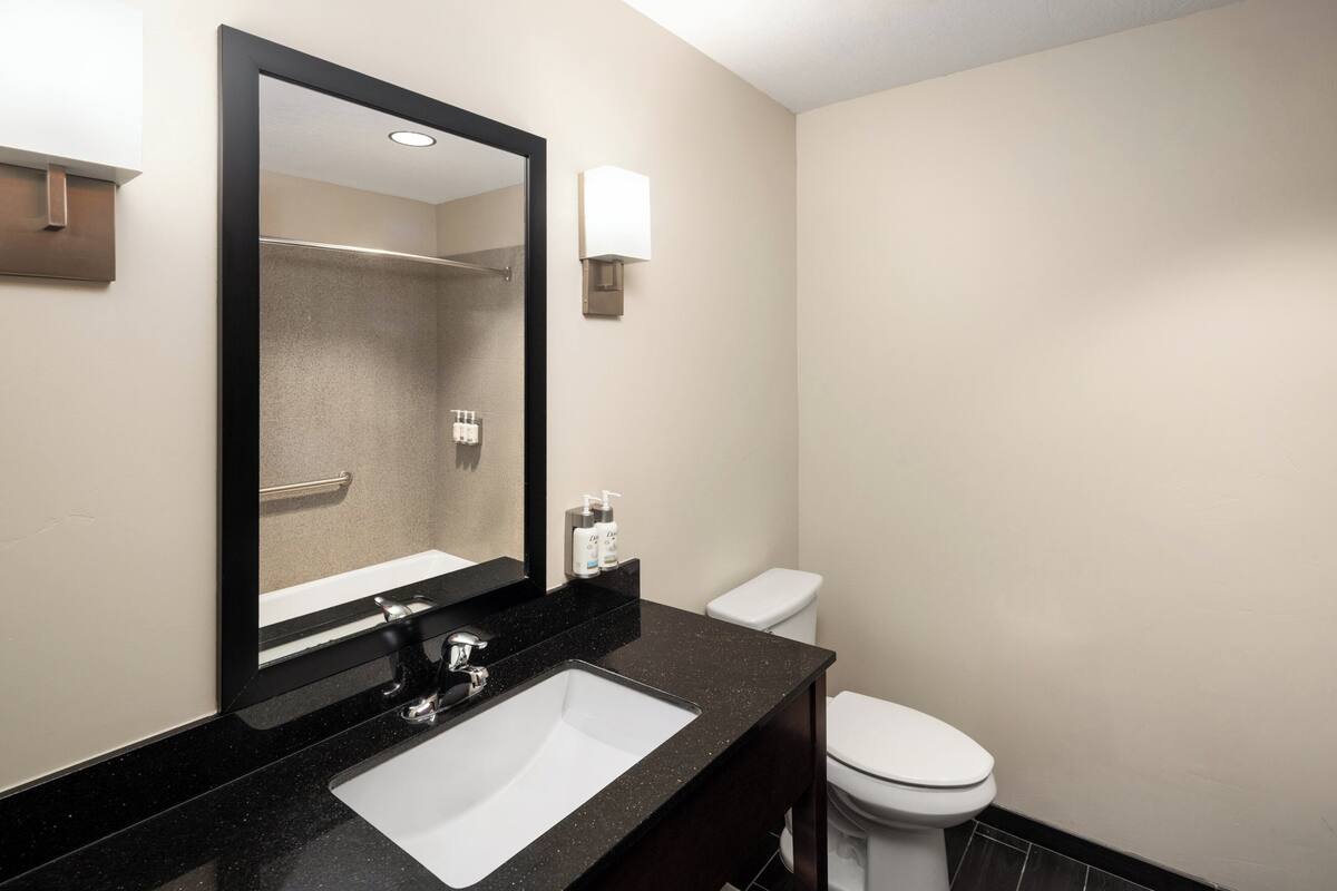 Une salle de bain avec un lavabo à vasque et un plan de toilette noirs, un miroir, des toilettes blanches et un porte-serviettes.