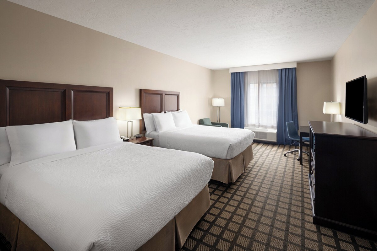 A hotel room with two beds, a desk, a chair, a TV, and a window with curtains.