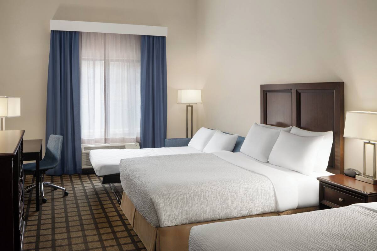 Une chambre d’hôtel avec deux lits, un bureau, une chaise et une lampe.