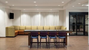 A modern dining area with a long table and six chairs, a sofa, and a television on the wall.