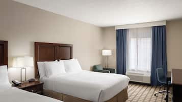A hotel room with two beds, a desk, a chair, a lamp, and a window with curtains.