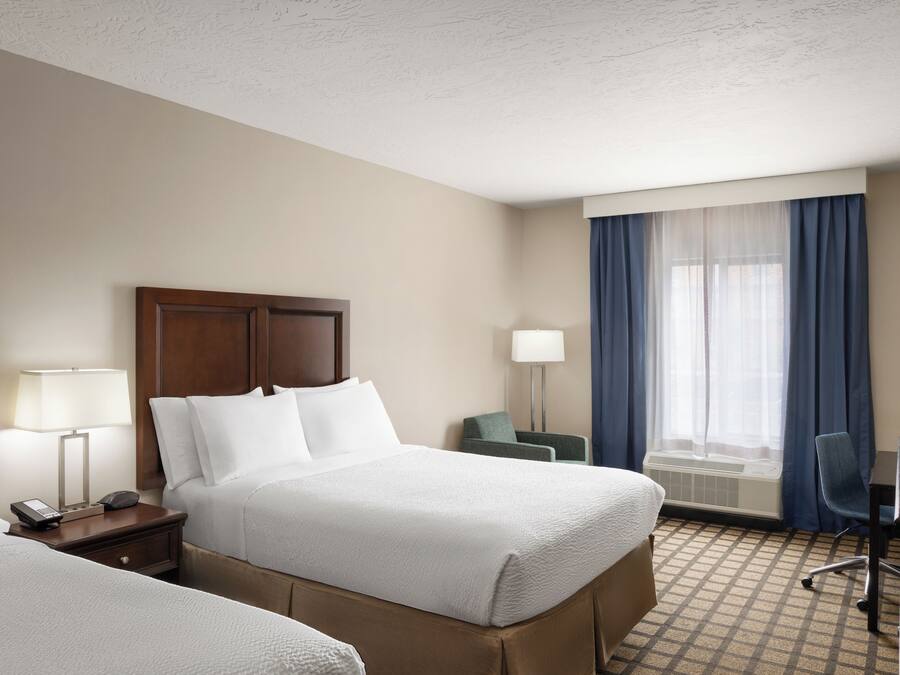 A hotel room with two beds, a desk, a chair, a lamp, and a window with curtains.