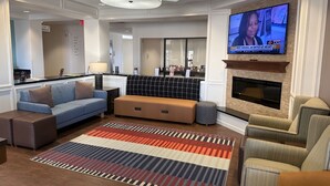 A modern living room with a sofa, ottoman, and armchair, a fireplace, a television, and a patterned rug.